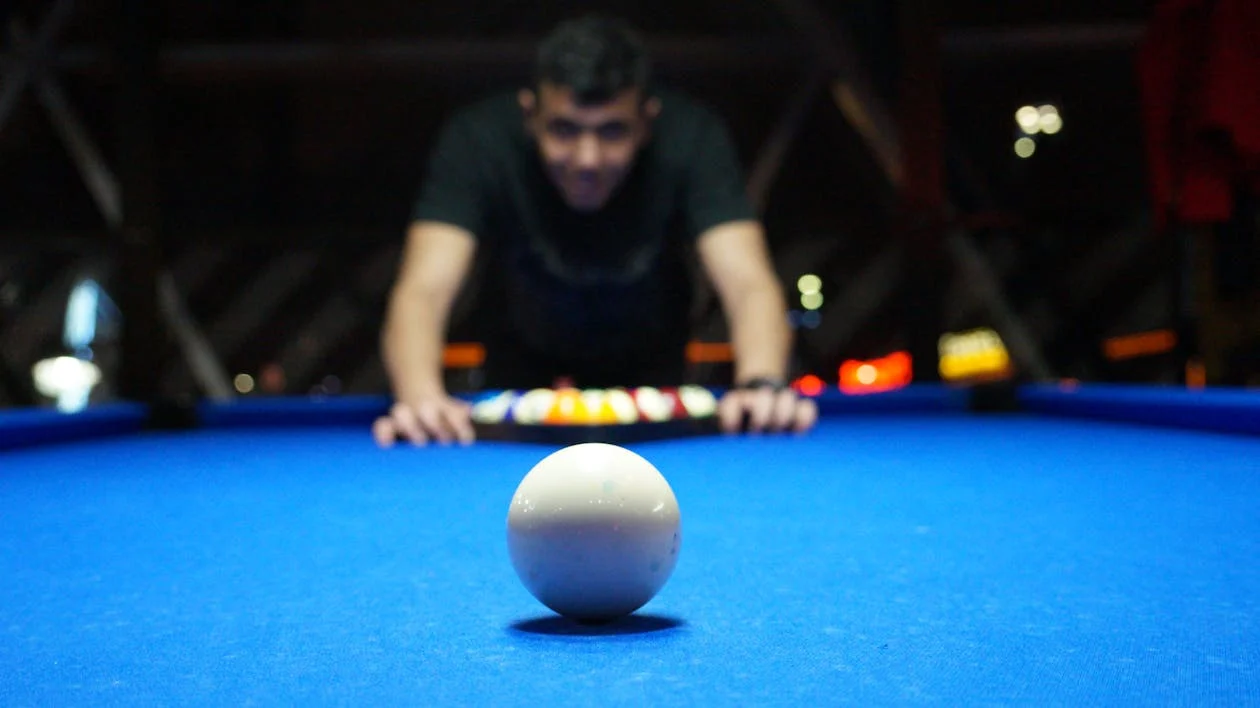 Man playing pool table while sharply looking at the white ball